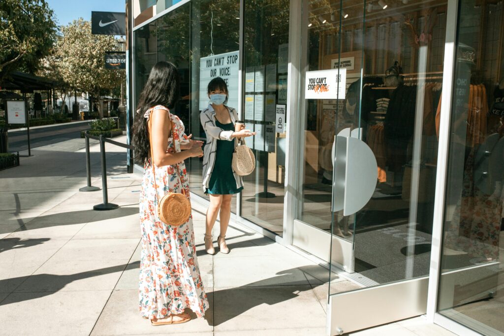 Two women social distancing outside a store during the daytime, highlighting shopping safety practices.