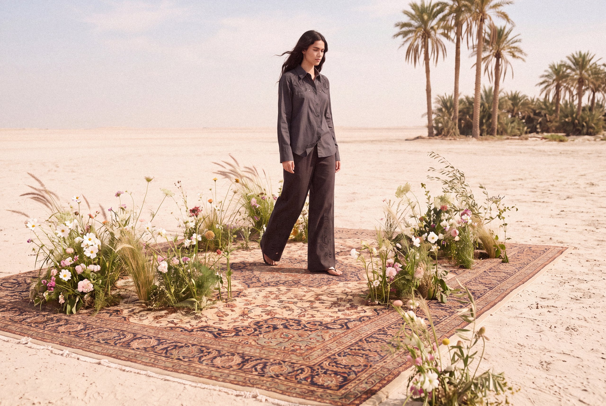 KINSHIP campaign: model in a dark coordinated outfit among flowers and desert palms