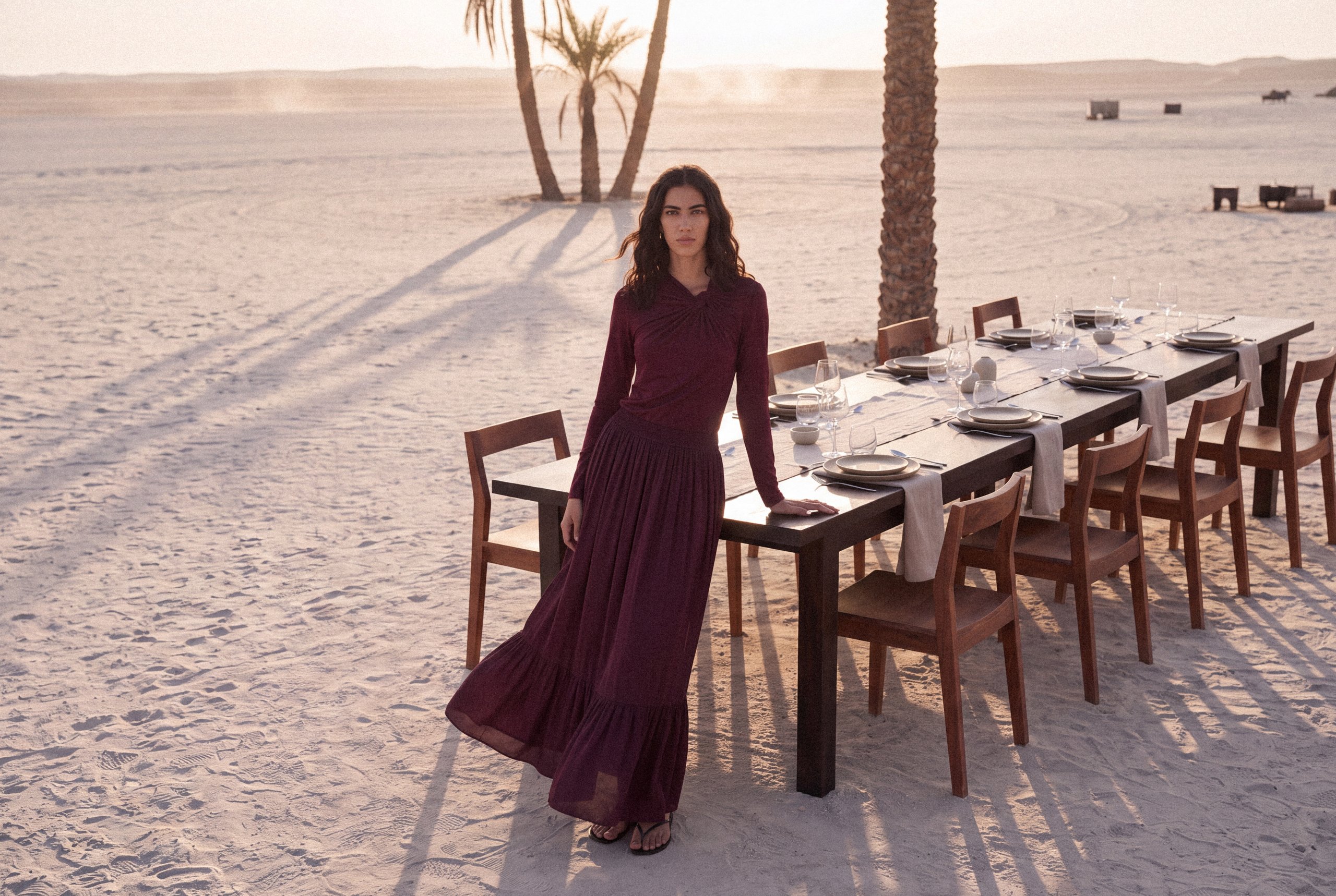 KINSHIP campaign: model in a burgundy dress beside a desert dining table